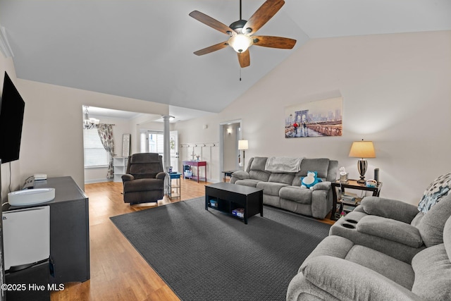 living room with decorative columns, ceiling fan with notable chandelier, light wood finished floors, and high vaulted ceiling