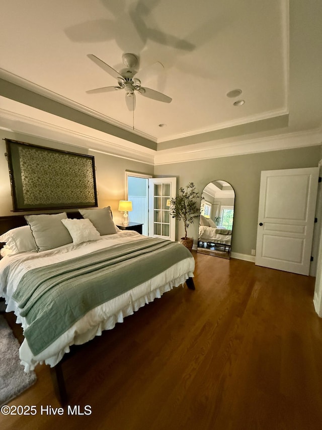 bedroom featuring baseboards, ornamental molding, wood finished floors, and a raised ceiling