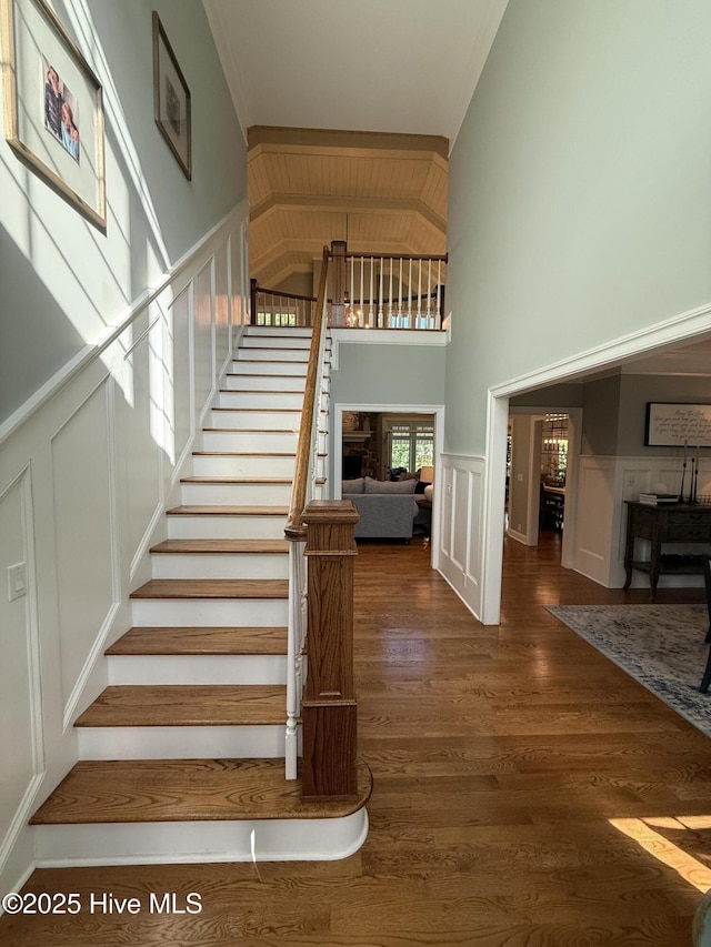 stairs with wood finished floors, wainscoting, and a decorative wall
