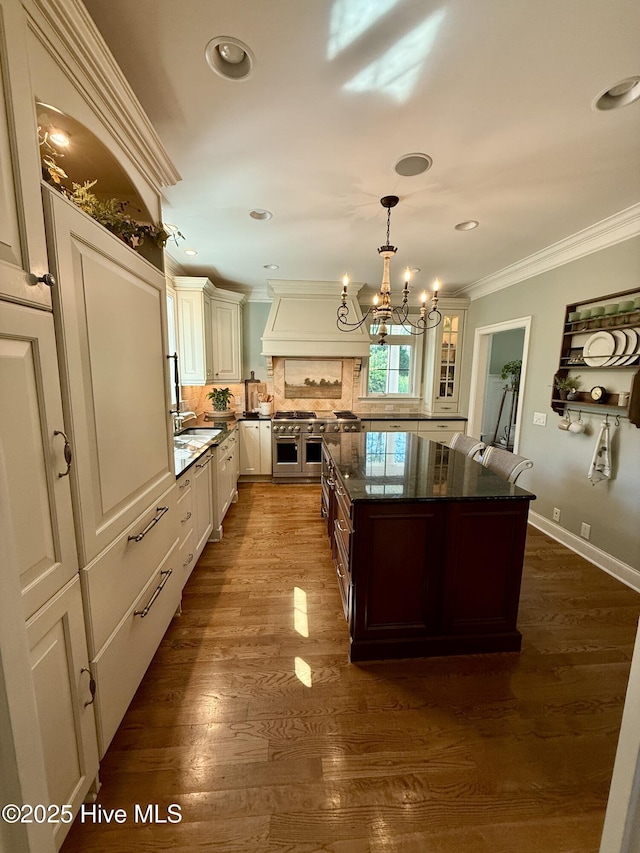 kitchen featuring crown molding, decorative backsplash, an inviting chandelier, custom range hood, and double oven range