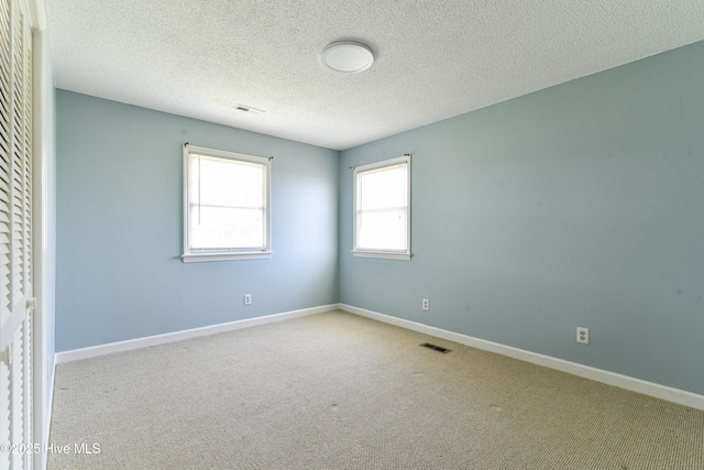 carpeted empty room with baseboards, a textured ceiling, and visible vents