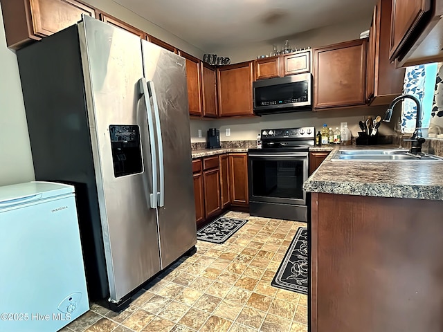 kitchen with stainless steel appliances, dark countertops, stone finish floor, and a sink