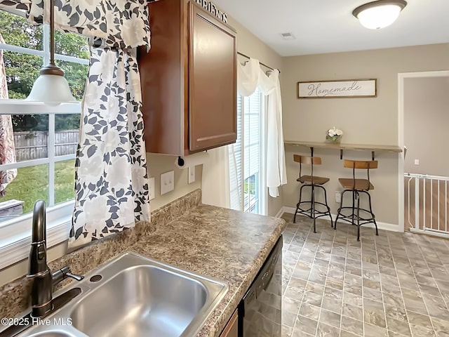 kitchen featuring a sink, stone finish floor, a breakfast bar, and dishwashing machine