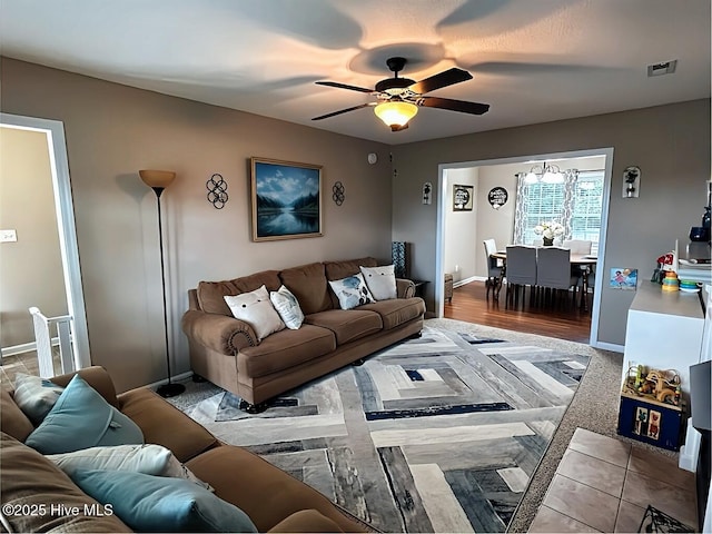 living room with baseboards, visible vents, and ceiling fan with notable chandelier