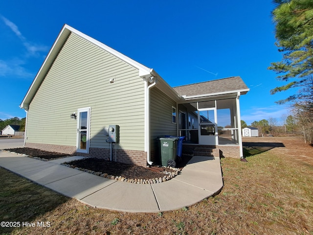 back of house with a sunroom, a shingled roof, a yard, and brick siding