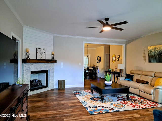 living room with ornamental molding, dark wood finished floors, a ceiling fan, baseboards, and a stone fireplace