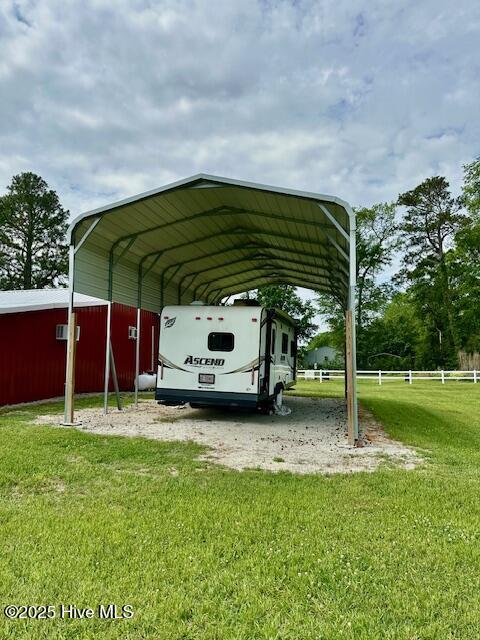 view of parking with fence, driveway, and a carport