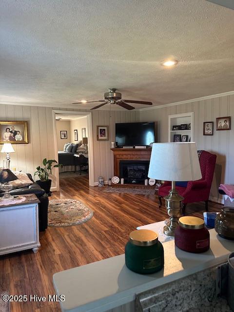 living area with a fireplace with raised hearth, a ceiling fan, a textured ceiling, and wood finished floors