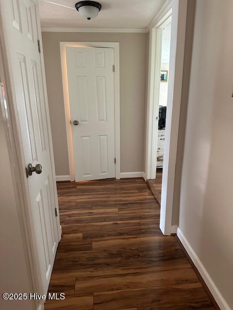 hallway featuring baseboards, ornamental molding, and dark wood-type flooring