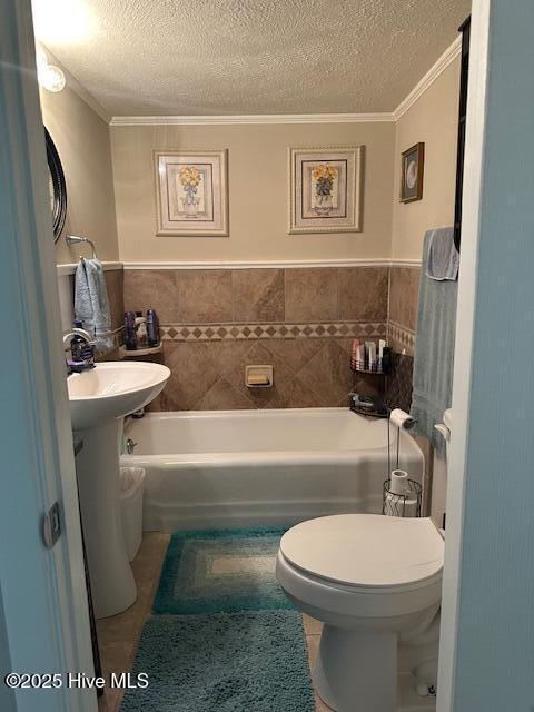 bathroom featuring toilet, a textured ceiling, a washtub, and ornamental molding