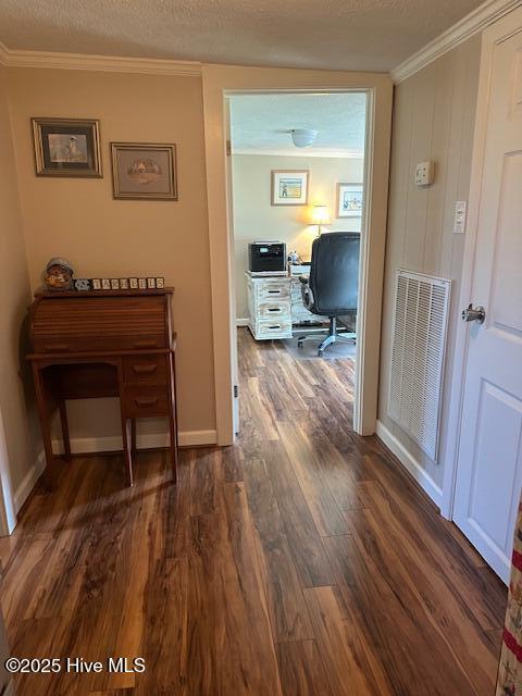 hallway with dark wood-style flooring, a textured ceiling, baseboards, visible vents, and ornamental molding