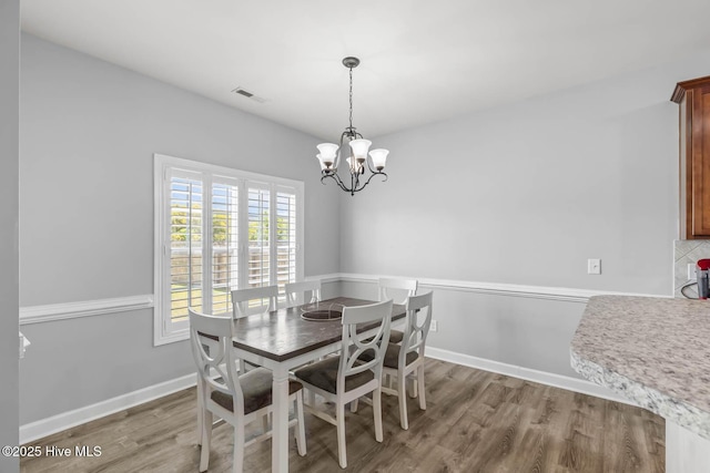 dining area featuring a chandelier, baseboards, visible vents, and wood finished floors