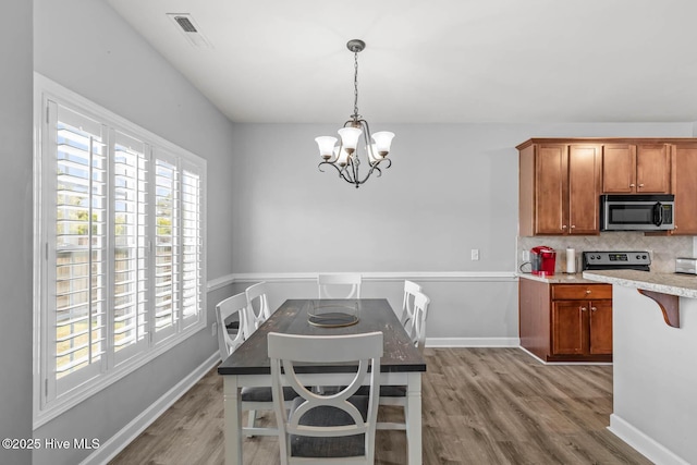 kitchen featuring visible vents, an inviting chandelier, wood finished floors, brown cabinets, and stainless steel appliances