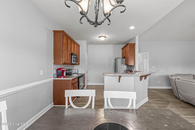 kitchen featuring appliances with stainless steel finishes, a notable chandelier, brown cabinets, and a breakfast bar