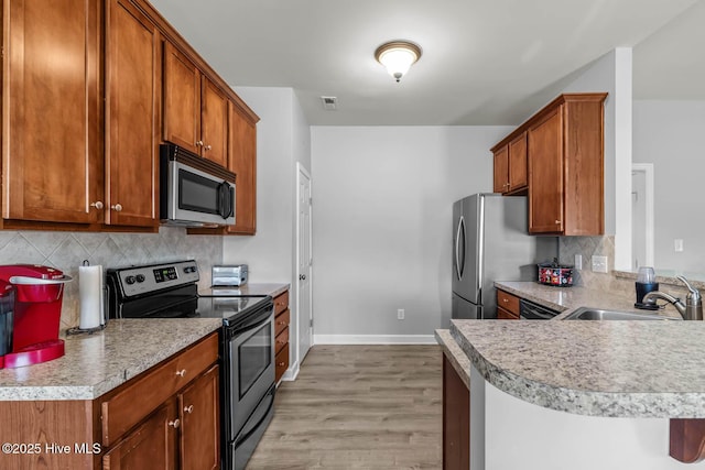 kitchen featuring brown cabinets, appliances with stainless steel finishes, light wood finished floors, baseboards, and tasteful backsplash