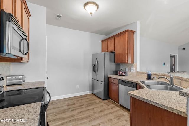 kitchen with brown cabinetry, backsplash, appliances with stainless steel finishes, light wood-type flooring, and a sink