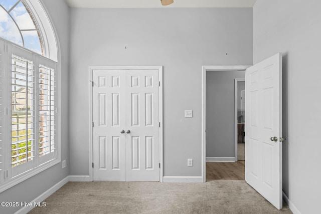 unfurnished bedroom with carpet floors, baseboards, a towering ceiling, and a closet