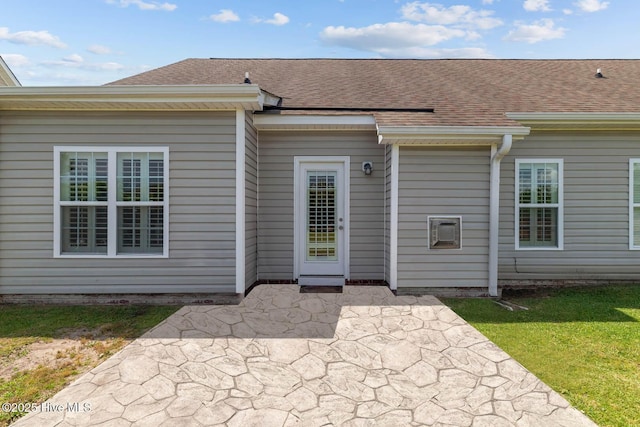 entrance to property with a shingled roof and a patio area