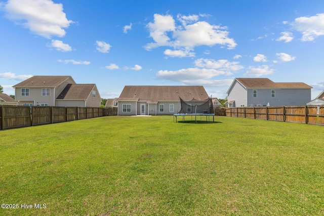 rear view of house featuring a fenced backyard, a trampoline, a yard, and a residential view