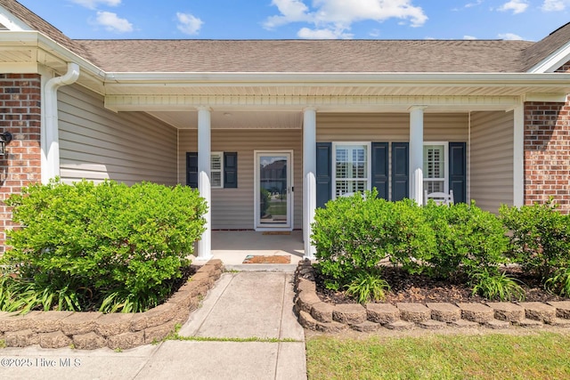 entrance to property featuring a porch, brick siding, and roof with shingles