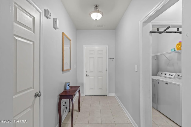 corridor with visible vents, baseboards, light tile patterned floors, and washing machine and clothes dryer