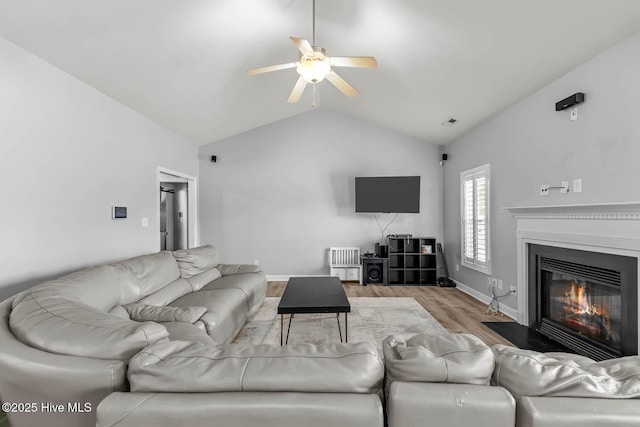 living room featuring visible vents, a ceiling fan, wood finished floors, a fireplace with flush hearth, and vaulted ceiling