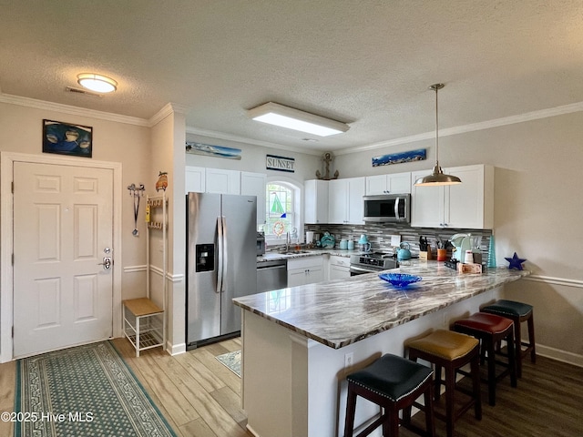 kitchen with stainless steel appliances, white cabinetry, a peninsula, light wood-type flooring, and a kitchen bar