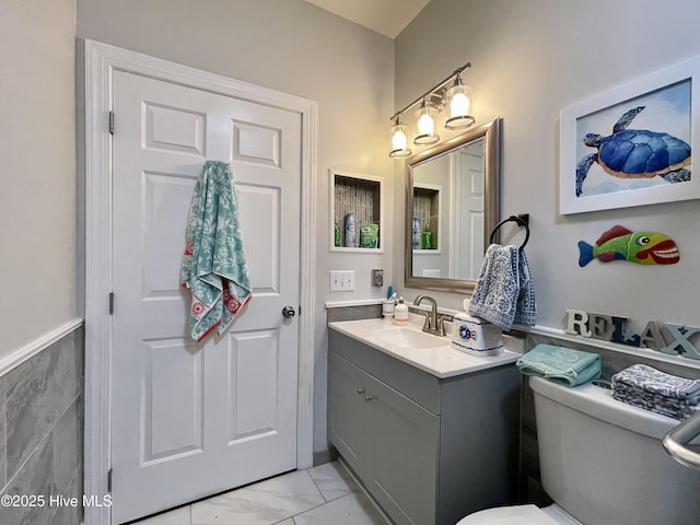 half bath featuring vanity, marble finish floor, and toilet