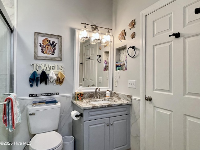 bathroom featuring toilet, tile walls, wainscoting, and vanity