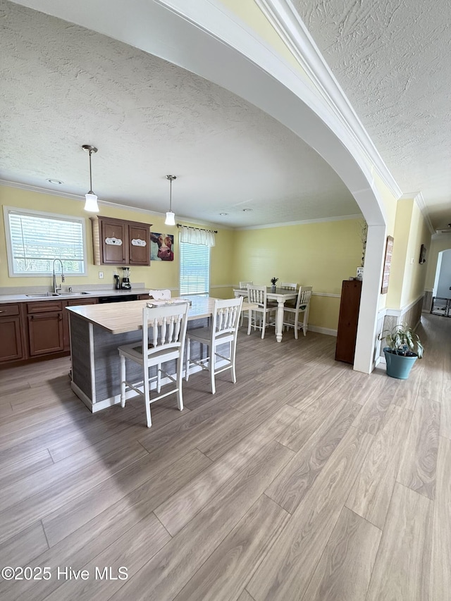 dining area featuring a textured ceiling, plenty of natural light, arched walkways, light wood-style floors, and ornamental molding