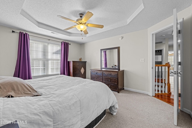 carpeted bedroom with a raised ceiling, a textured ceiling, baseboards, and a ceiling fan