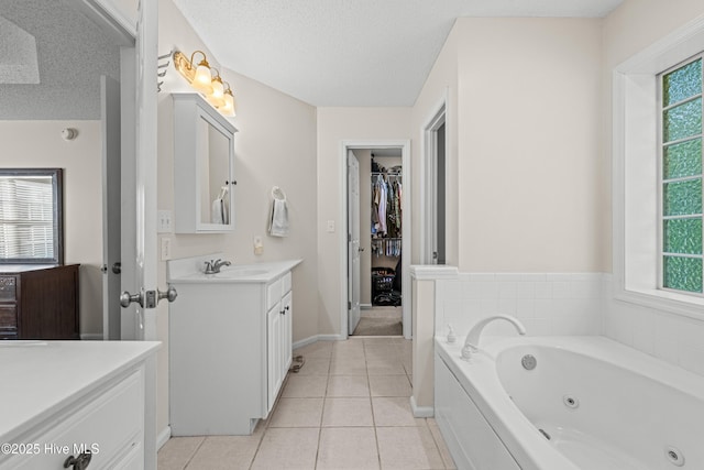 bathroom featuring vanity, plenty of natural light, tile patterned flooring, a tub with jets, and a textured ceiling
