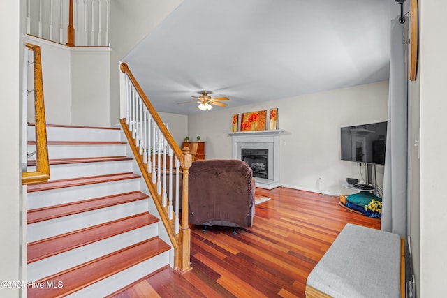 staircase with a ceiling fan, wood finished floors, a glass covered fireplace, and baseboards