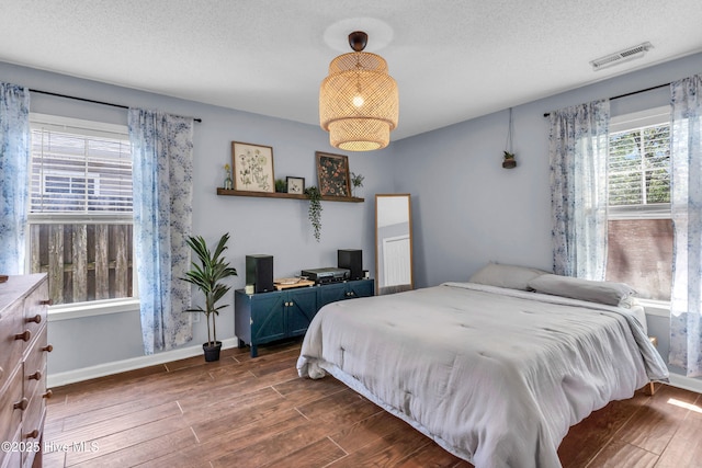 bedroom with visible vents, a textured ceiling, baseboards, and dark wood-style floors