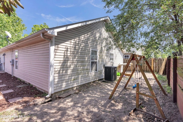 view of property exterior with central AC unit, a playground, and fence