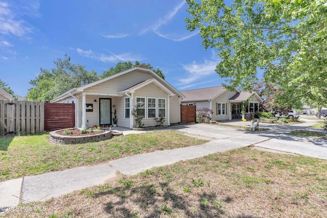 view of front of property with a front lawn, fence, covered porch, an attached garage, and driveway
