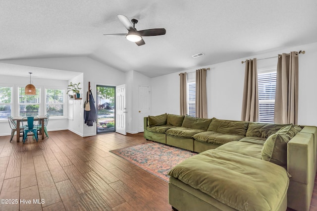 living room featuring ceiling fan, a textured ceiling, vaulted ceiling, visible vents, and dark wood-style floors