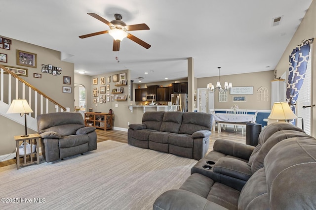 living room with visible vents, baseboards, stairway, light wood finished floors, and ceiling fan with notable chandelier