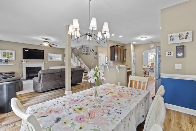dining room featuring light wood-style floors, a glass covered fireplace, ceiling fan with notable chandelier, recessed lighting, and baseboards