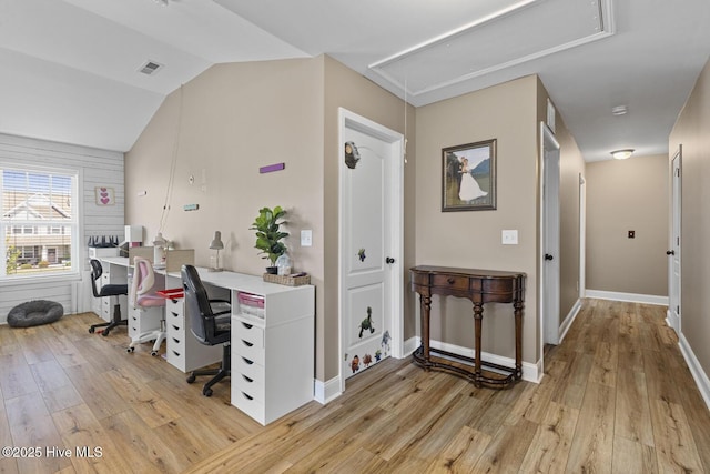 office space featuring visible vents, light wood-style flooring, attic access, baseboards, and vaulted ceiling