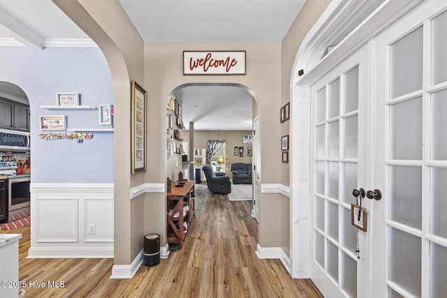 hall with light wood-type flooring, arched walkways, and baseboards