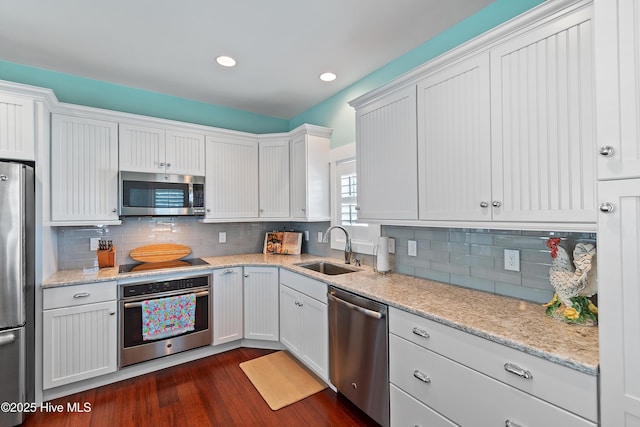kitchen with appliances with stainless steel finishes, a sink, white cabinets, dark wood-type flooring, and recessed lighting