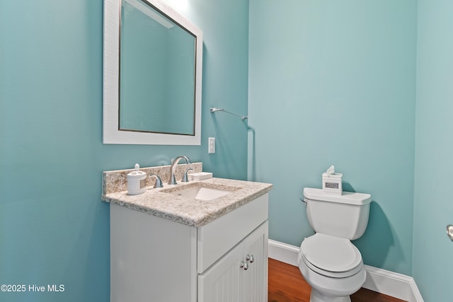 half bath with wood finished floors, vanity, baseboards, and toilet