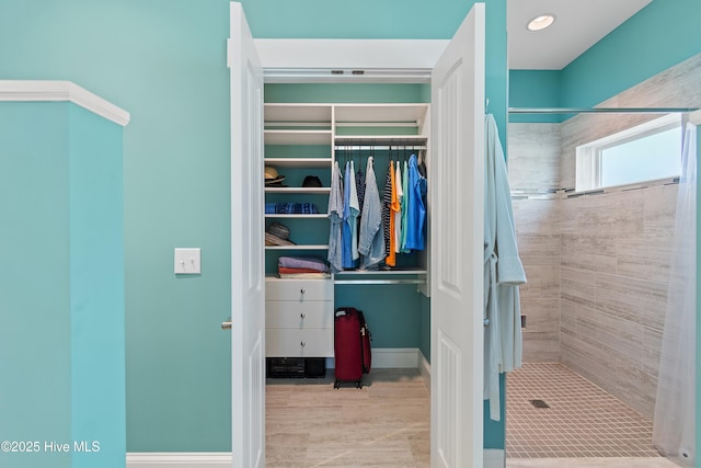 full bathroom featuring a stall shower, a spacious closet, and baseboards