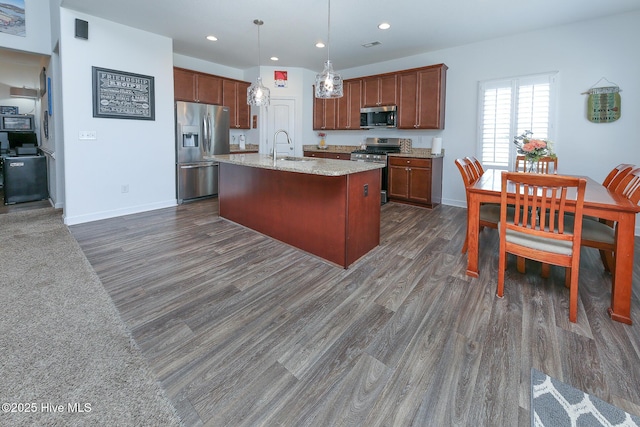 kitchen featuring appliances with stainless steel finishes, dark wood finished floors, a sink, pendant lighting, and an island with sink