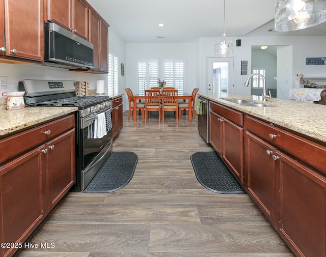 kitchen with appliances with stainless steel finishes, a sink, wood finished floors, light stone counters, and recessed lighting