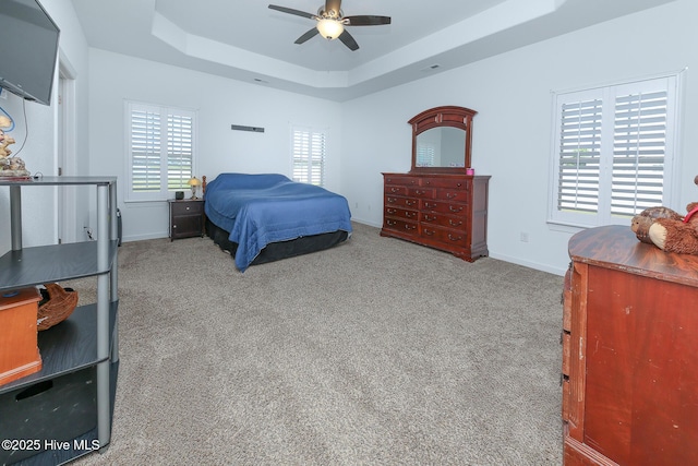 carpeted bedroom with a raised ceiling, multiple windows, baseboards, and a ceiling fan