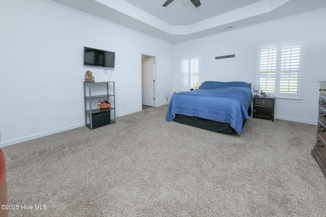 carpeted bedroom with a raised ceiling, multiple windows, baseboards, and ceiling fan