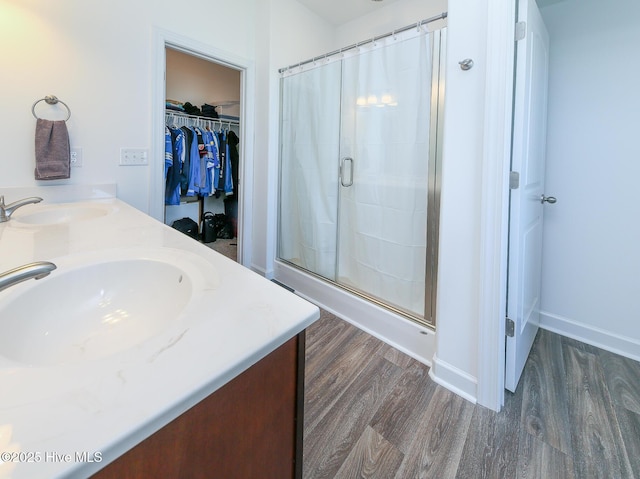 full bathroom with wood finished floors, a stall shower, double vanity, and a walk in closet