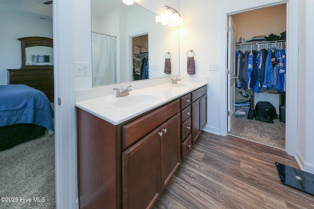 bathroom with wood finished floors, double vanity, a walk in closet, and connected bathroom